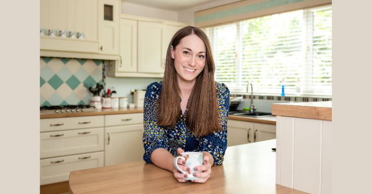 image shows Kate, a woman with long brown hair smiling at the camera in a kitchen